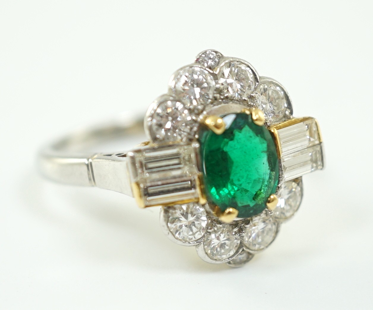 A modern platinum, oval cut emerald and baguette and round cut diamond set cluster ring